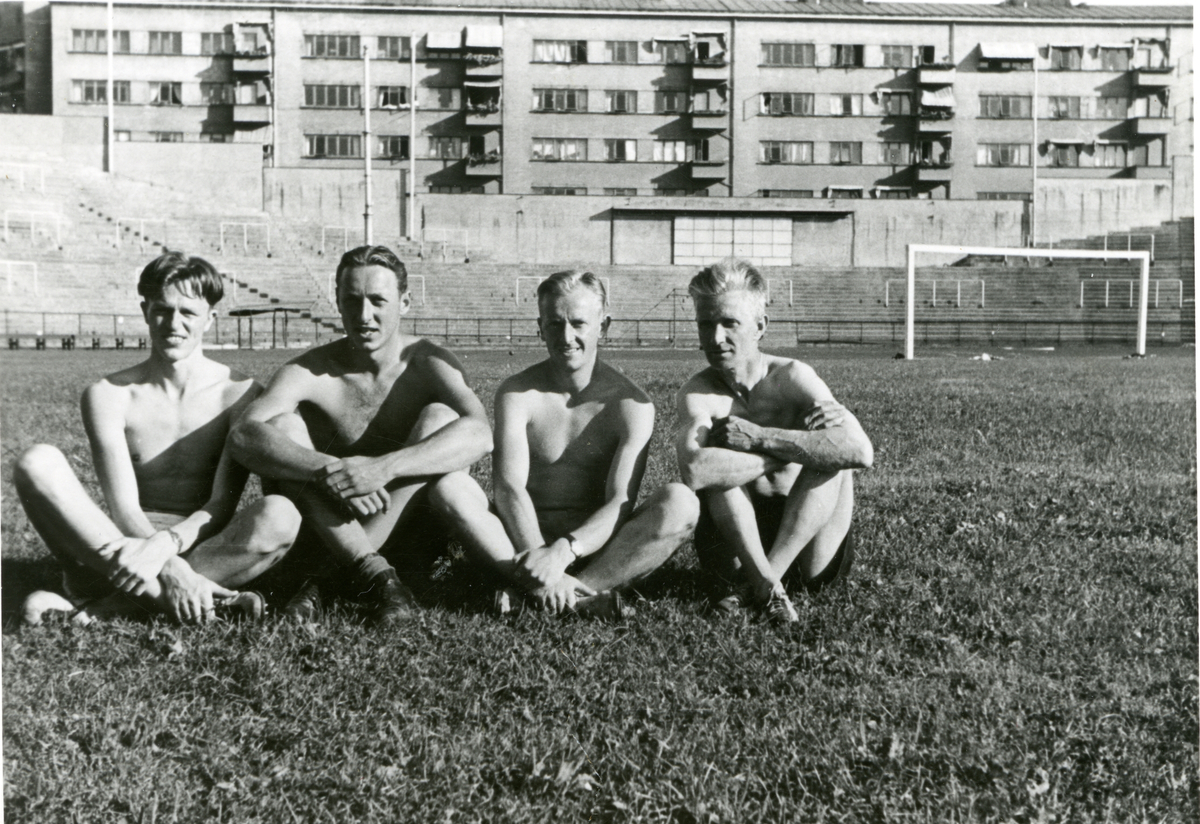 Fire unge menn sitter på en fotballbane, med boligblokker i bakgrunnen ...