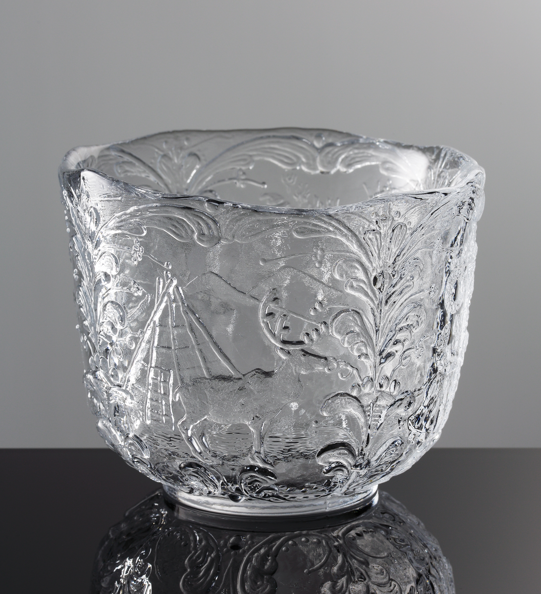 Formgiven av Kjell Engman. Reliefmönster i form av fyra olika typiska svenska motiv mellan stående kurbitsmönster: Nils Holgersson, statshuset, en kåta och en ren, midsommarstång med dans.