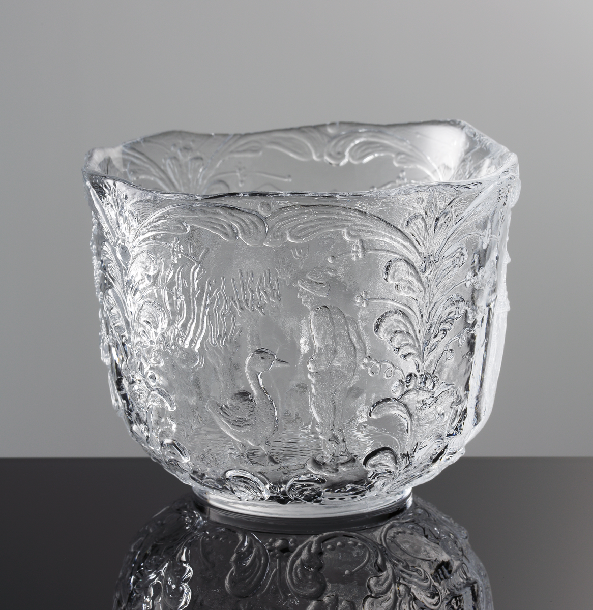 Formgiven av Kjell Engman. Reliefmönster i form av fyra olika typiska svenska motiv mellan stående kurbitsmönster: Nils Holgersson, statshuset, en kåta och en ren, midsommarstång med dans.