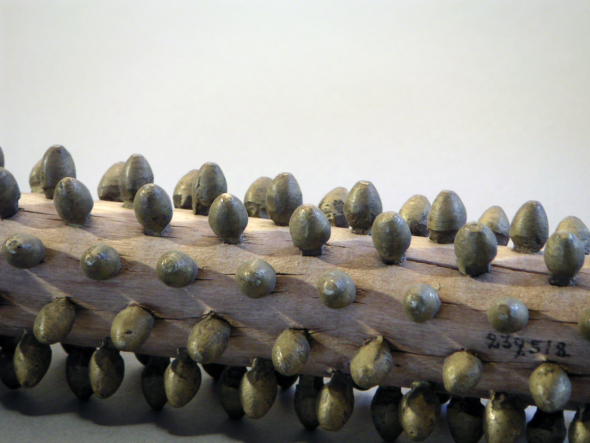 Rullnagg, för spisbröd. Rader av mässingsnaggar, trärulle som sitter i järnfattning, vilket har svarvat träskaft. Trasig, har lossnat från skaftet. Sprucken. 