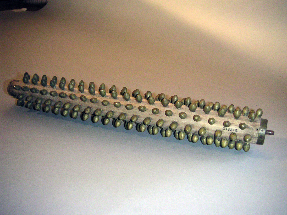 Rullnagg, för spisbröd. Rader av mässingsnaggar, trärulle som sitter i järnfattning, vilket har svarvat träskaft. Trasig, har lossnat från skaftet. Sprucken. 