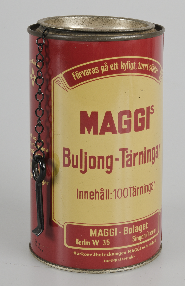 Burk av röd- och gulmålad plåt, med text, bl. a: "MAGGIS  Buljong-Tärningar Innehåll: 100 Tärningar". På burkens överkant hänger en öppnare. Locket kan öppnas och förslutas. Burken är tom.


