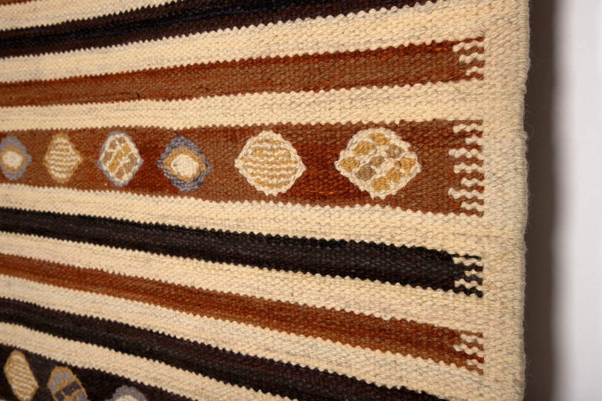 Gulvteppet vevd i röllakanteknikk. Lingarn i renningen og nauthårsgarn i innslaget. Stripet i hvitt, rødbrunt og brunsvart i innlagsretningen, sju smale striper veksler med en bredere stripe hver 25. cm. I de brede stripene er det vevd inn spissovale former med hvitt, lilla og gult fylldekor bestående av avvekslende flekker, striper og spissovaler. På langsidene en 3 cm bred jarekant i hvitt. I teppets kortender er det knyttet frynser av renningen.