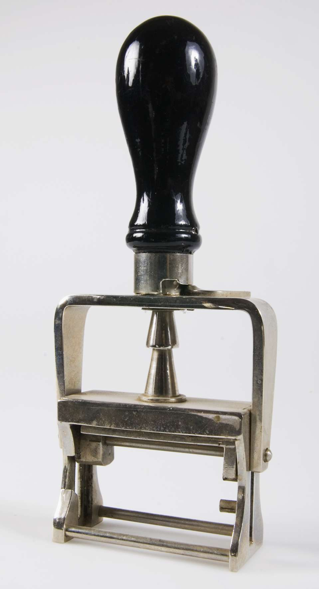 Stämpel av förkromat järn med svart svarvat trähandtag. Stämpel av gummi med texten: "Lennaholm A.B.". Stämpelytan vilar mot en gredelin stämpeldyna och vänds när stämpeln pressas ned. Kan låsas i nedtryckt läge med en spak.
