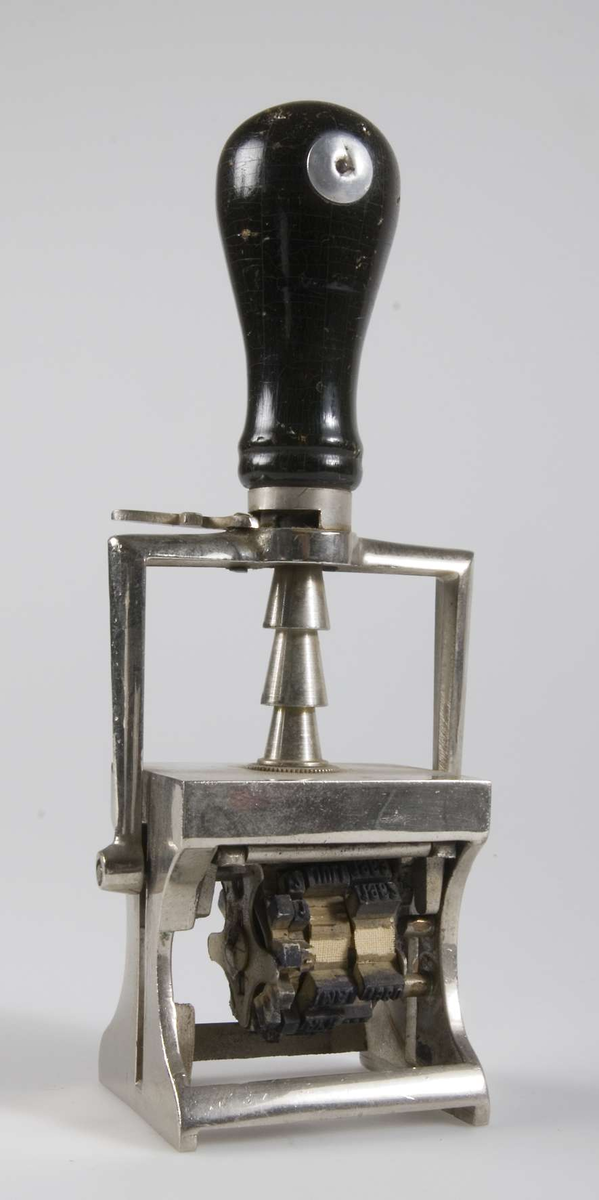 Stämpel av förkromat järn med svart svarvat trähandtag. Dels datumstämpel av gummi med årtal från 1950 och 60-talet dels stämpel för ankommande post som vilar mot stämpeldyna och vänds ner när stämpeln pressas ned. 
