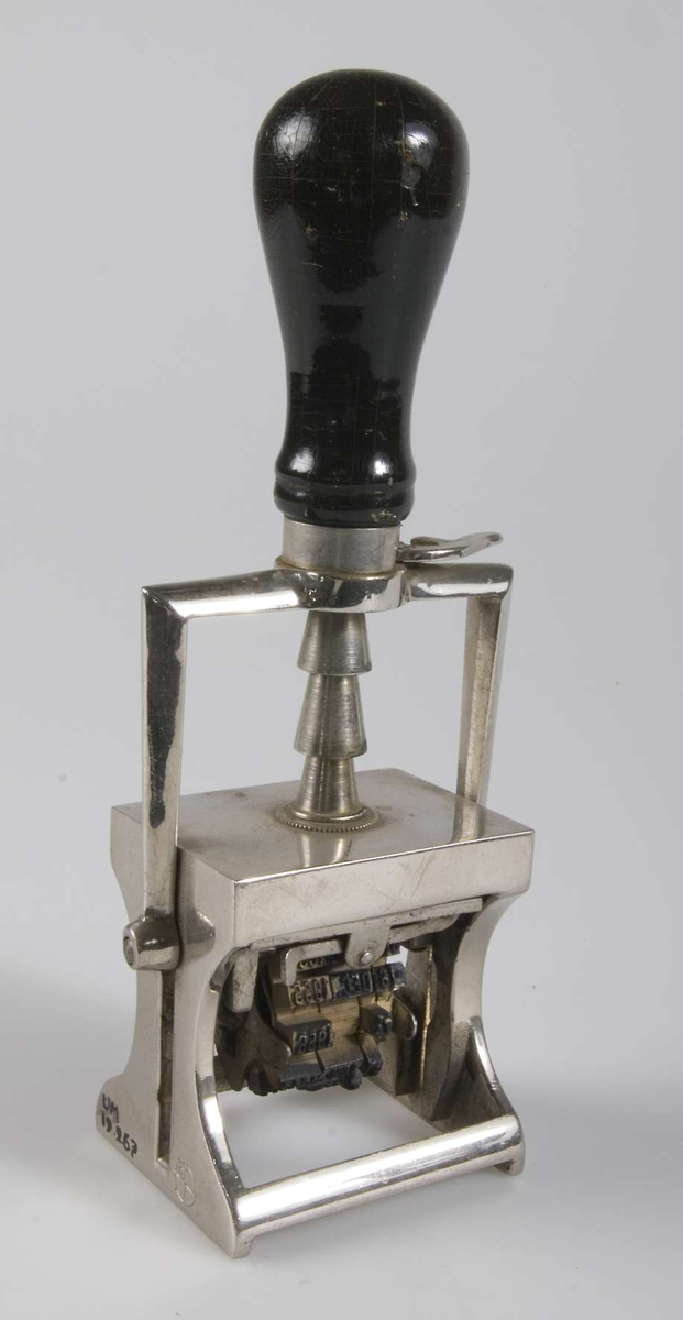 Stämpel av förkromat järn med svart svarvat trähandtag. Dels datumstämpel av gummi med årtal från 1950 och 60-talet dels stämpel för ankommande post som vilar mot stämpeldyna och vänds ner när stämpeln pressas ned. 
