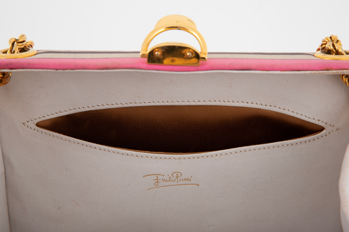 Liten boksveske med ett stort innerrom og et mindre innerrom på bakveggen. Vesken er hard, og må ha en innvendig kjerne av et hardt materiale. Utvendig er den trukket med et silketrykk i sterke rosa nyanser, nonfigurativt, men likevel noe geometrisk av type. Mønstertypen er karakteristisk for designeren Emilio Pucci på sluttet av 1960-tallet og på 1970-tallet. Innvendig kledd med hvitt kidskinn, og stor, båtformet åpning på innerlommen. Innerrommet er fôret med bronsefarget skinn. Knepplås på midten av oversiden og 2 bærelenker, tredd gjennom kraftige maljer på toppen og øverst på kortsidene. De tvunne "gullenkene" holdes på plass av små kuler i endene. På undersiden, 4 små halvkuleformede ben av samme metall.