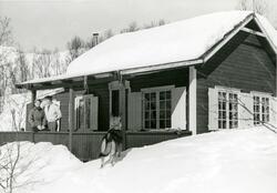 Mann og kvinne står på verandaen utenfor et hus i vinterlandskap
