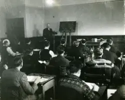 Undervisning i eit klasserom ved Maskinistskulen i London under andre værdskrigen. Læraren i offisersuniform og elevane i daglegdags påkledning.