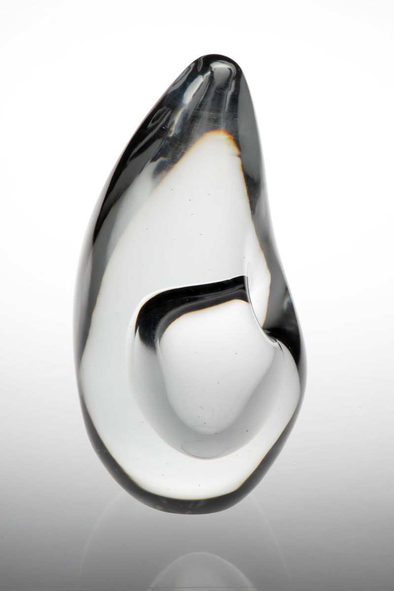 Dråpeformet skulpturell vase med abstrakt utforming i massivt klart glass. Et ellipseformet hulerom i nedre del med liten sirkulær åpning. Bunnen er planslipt.