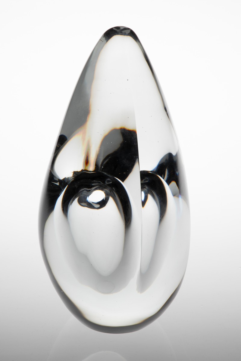 Dråpeformet skulpturell vase med abstrakt utforming i massivt klart glass. Et ellipseformet hulerom i nedre del med liten sirkulær åpning. Bunnen er planslipt.