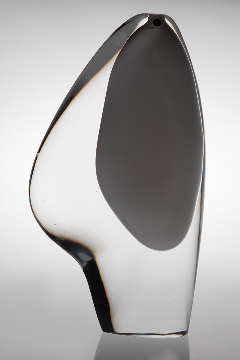 Skiveformet vase med en abstrakt, skulpturell utforming i underfangsglass. Det innerste sjiktet består av opakt melkehvitt glass som danner et tilnærmet elipseformet hulerom, mens det ytre sjiktet er i klart glass.