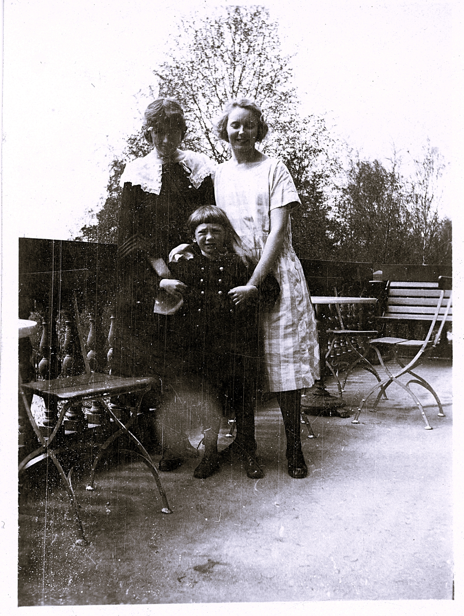 Foto av Lill-Olle på balkongen med Margit (enligt bildtext i album). Text baksida kort: "Margit är kassa, Hedvig är uppasserska och Olle".