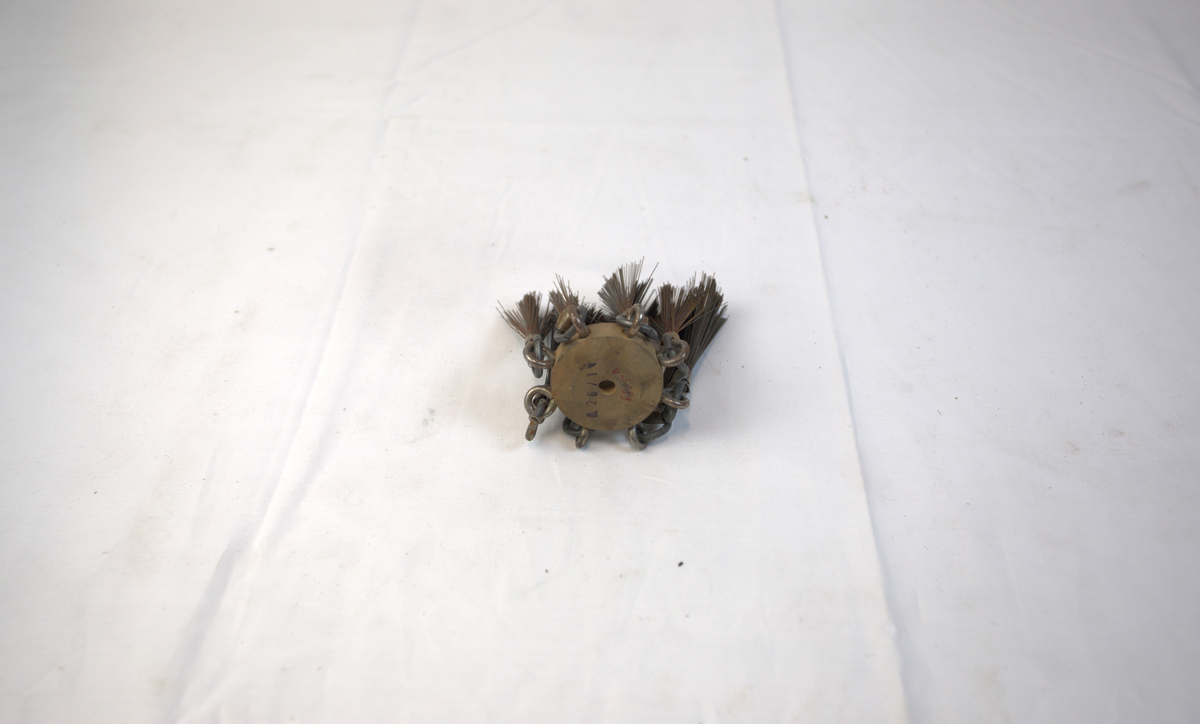 Polerstikkel brukt i gullsmedvirksomhet. I midten er det en sirkelformet gjenstand i tre. I denne er det festet åtte stålbørster.