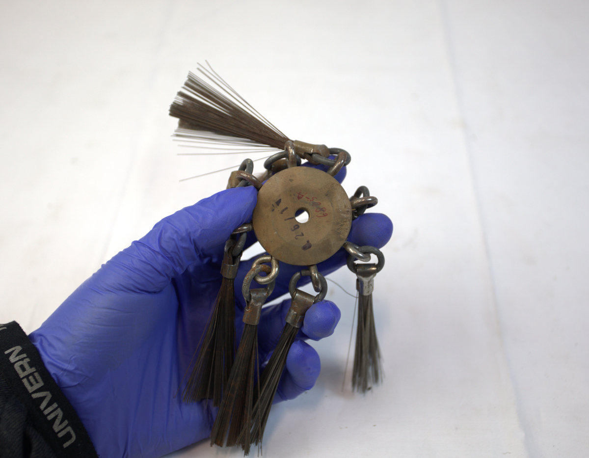 Polerstikkel brukt i gullsmedvirksomhet. I midten er det en sirkelformet gjenstand i tre. I denne er det festet åtte stålbørster.