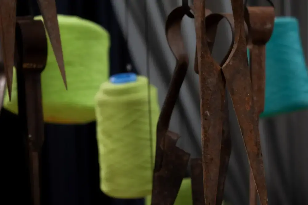 Nærbilde av rustne sauesakser og store spoler grønn ulltråd som henger fra taket i utstillingsrommet.