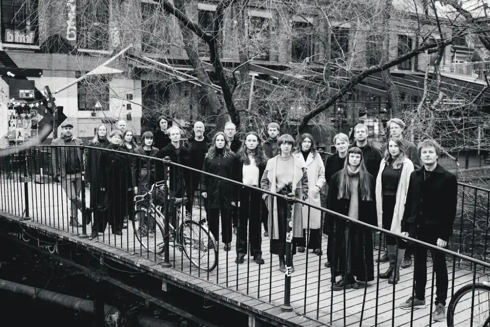 svart kvitt bilde av Oslo kammerkor som står på ei trebru