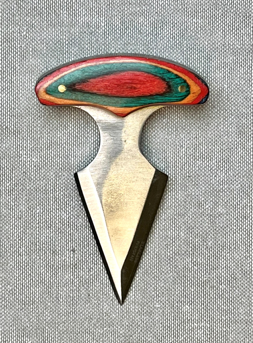 Trekantet tveegget kniv med T-formet flerfarget håndtak i tre. Slire i kunstskinn preget med en ørnefigur. Sliren lukkes med en trykknapp.