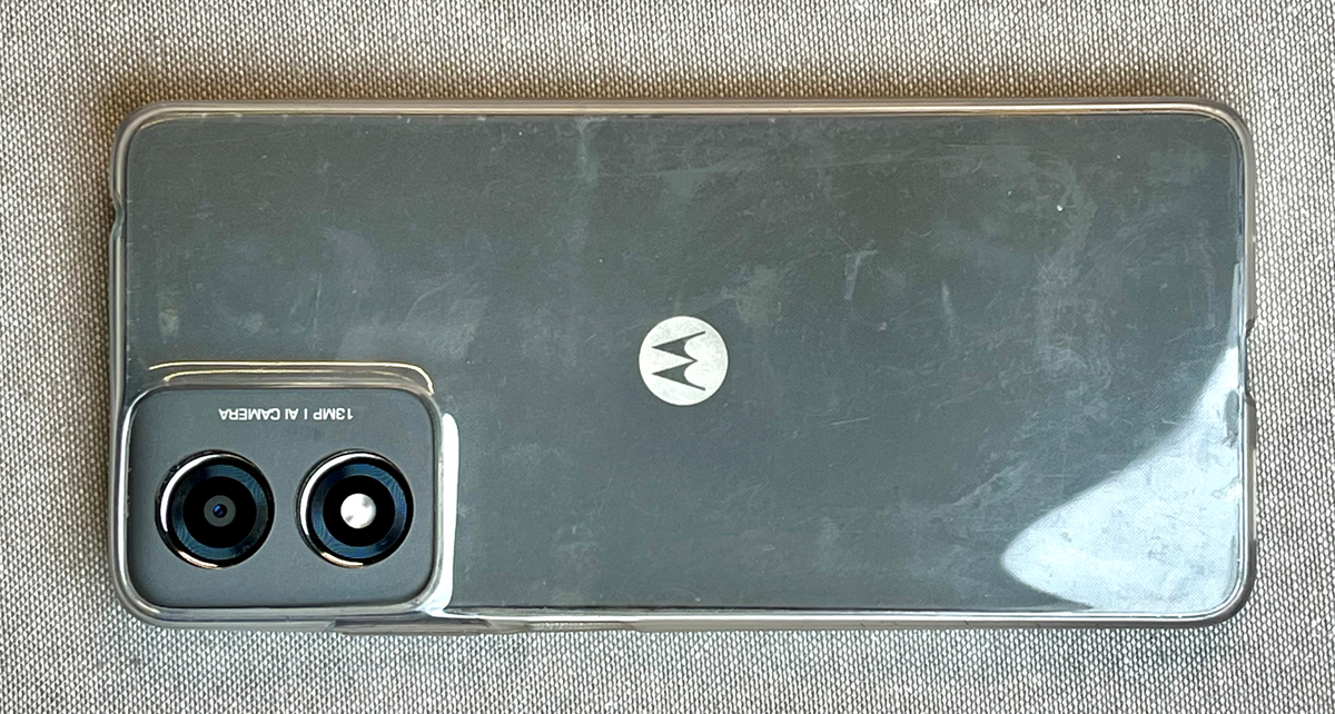 Grå smarttelefon med beskytelsescover i gjennomsiktig gummi. Telefonen har store skader. Skjermen er knust, og selve telefonen er bøyd. Simkort og batteri er fjernet.