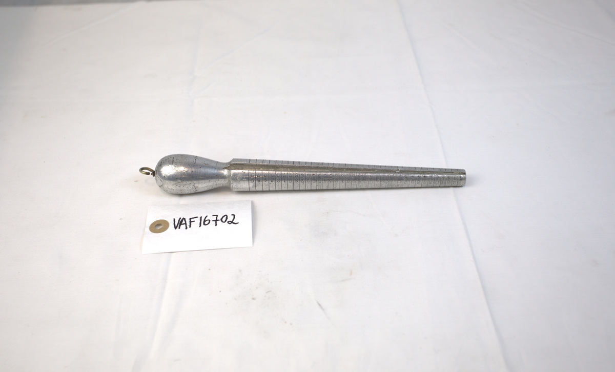 Verktøy til bruk for å lage ringer. Den har striper som går rundt den tilspissede delen. På den ene siden er det også tall i stigende rekkefølge. 