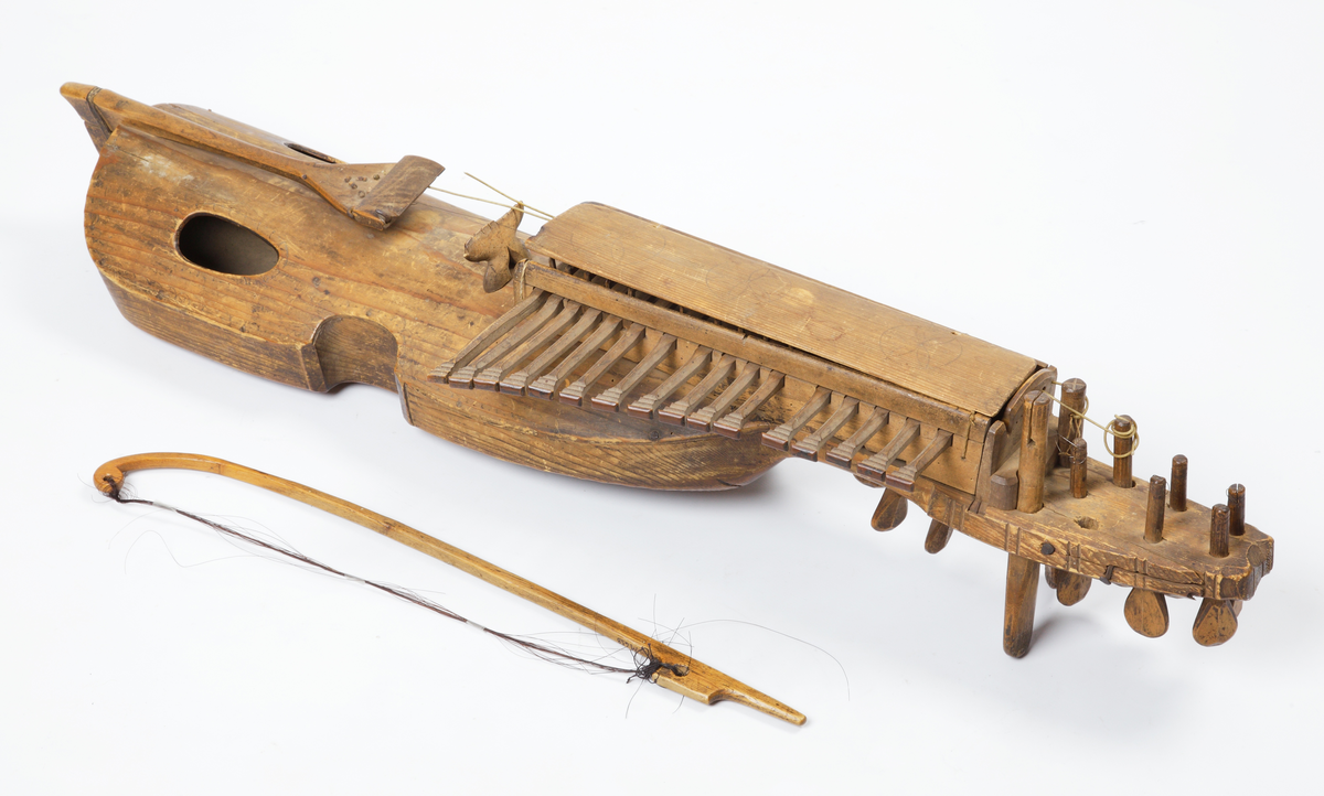 Nyckelharpa med tillhörande stråke. Tillverkad av omålat trä. Kropp och hals är gjorda i ett stycke. Locket är kraftigt välvt och har två oval ljudhål. Nyckelharpan har sexton nycklar (knavrar) och har haft fjorton stämskruvar på halsen (en saknas). De flesta strängar saknas, även stallet. Den har ett lock ovanför nyckelmekanismen, som är dekorerat med tre cirklar, dragna med passare. Även sargen, ljudhålens kanter och strängfästet är dekorerade med passdragna halvcirklar. Stråken är kraftigt böjd och har en del av taglet kvar.