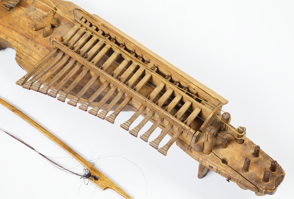 Nyckelharpa med tillhörande stråke. Tillverkad av omålat trä. Kropp och hals är gjorda i ett stycke. Locket är kraftigt välvt och har två oval ljudhål. Nyckelharpan har sexton nycklar (knavrar) och har haft fjorton stämskruvar på halsen (en saknas). De flesta strängar saknas, även stallet. Den har ett lock ovanför nyckelmekanismen, som är dekorerat med tre cirklar, dragna med passare. Även sargen, ljudhålens kanter och strängfästet är dekorerade med passdragna halvcirklar. Stråken är kraftigt böjd och har en del av taglet kvar.