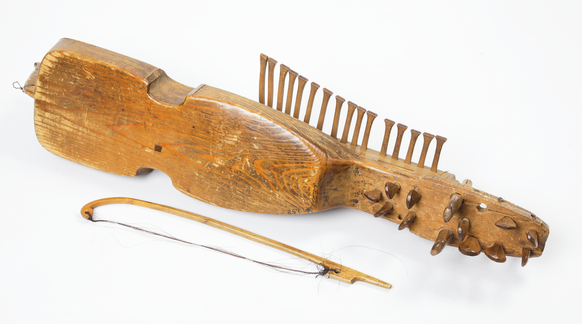 Nyckelharpa med tillhörande stråke. Tillverkad av omålat trä. Kropp och hals är gjorda i ett stycke. Locket är kraftigt välvt och har två oval ljudhål. Nyckelharpan har sexton nycklar (knavrar) och har haft fjorton stämskruvar på halsen (en saknas). De flesta strängar saknas, även stallet. Den har ett lock ovanför nyckelmekanismen, som är dekorerat med tre cirklar, dragna med passare. Även sargen, ljudhålens kanter och strängfästet är dekorerade med passdragna halvcirklar. Stråken är kraftigt böjd och har en del av taglet kvar.