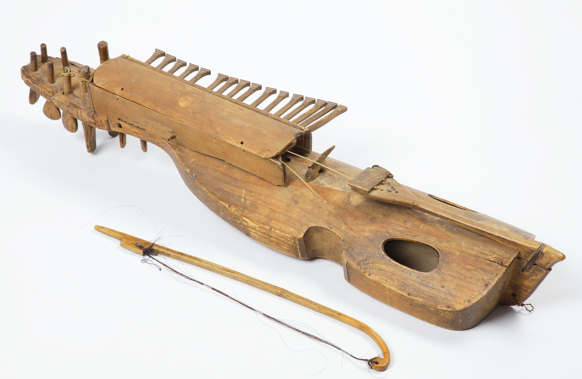 Nyckelharpa med tillhörande stråke. Tillverkad av omålat trä. Kropp och hals är gjorda i ett stycke. Locket är kraftigt välvt och har två oval ljudhål. Nyckelharpan har sexton nycklar (knavrar) och har haft fjorton stämskruvar på halsen (en saknas). De flesta strängar saknas, även stallet. Den har ett lock ovanför nyckelmekanismen, som är dekorerat med tre cirklar, dragna med passare. Även sargen, ljudhålens kanter och strängfästet är dekorerade med passdragna halvcirklar. Stråken är kraftigt böjd och har en del av taglet kvar.