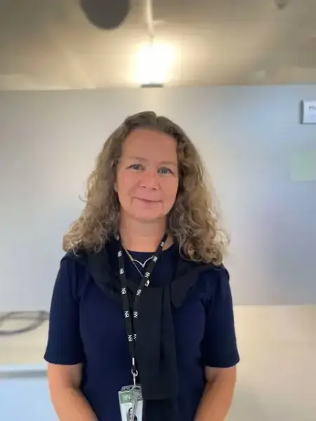 Fotografi av ei kvinne som ser inn i kamera. Hun har lyst småkrøllete hår, og en blå overdel.