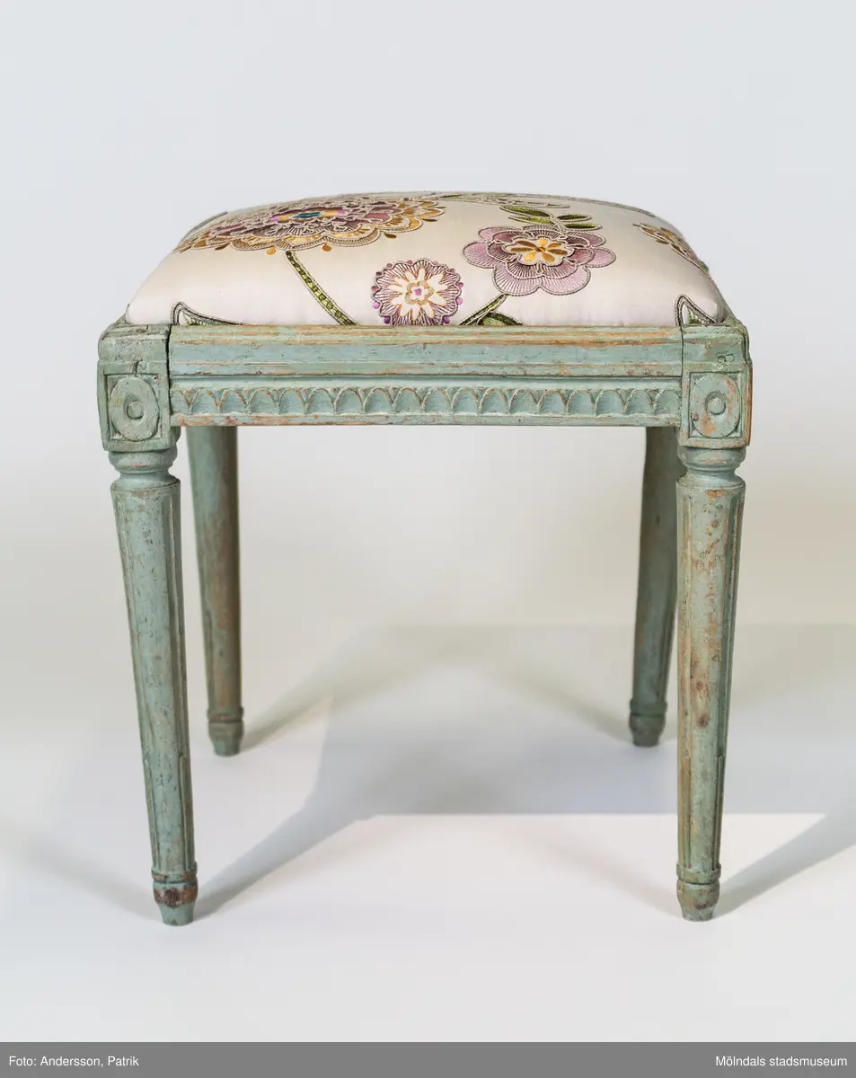 Taburett, gustaviansk, raka sarger med fjällskärning, svarvade ben med kanelyrer, benanfanger med en oval inskriven i en kvadrat, på insidan av sargen signerad IAS. Framtagen ljusgrön originalfärg. Omklädd 2013 med nytt tyg dekorerat med broderade blommor.

Taburetten är tillverkade i Lindome omkring 1790.
Signaturen IAS kan avse någon av stolmakarna Johnnes Andersson i Skå 1, (1763-1840) eller Johannes Andersson i Lindomeby 6, (1775-1855).