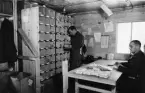 Svenska Frivilligkåren i Finland.  Fältpostkontor i Tornio,
1940.  Brevavdelningen.  Brevsorteraren.  Dagligen ankommo upp till
15 000 brev per dag under högkonjunkturen.  Sortering skedde på c:a
110 adresser.  Sittande: fältväbel Åsbrink, Helsinki.