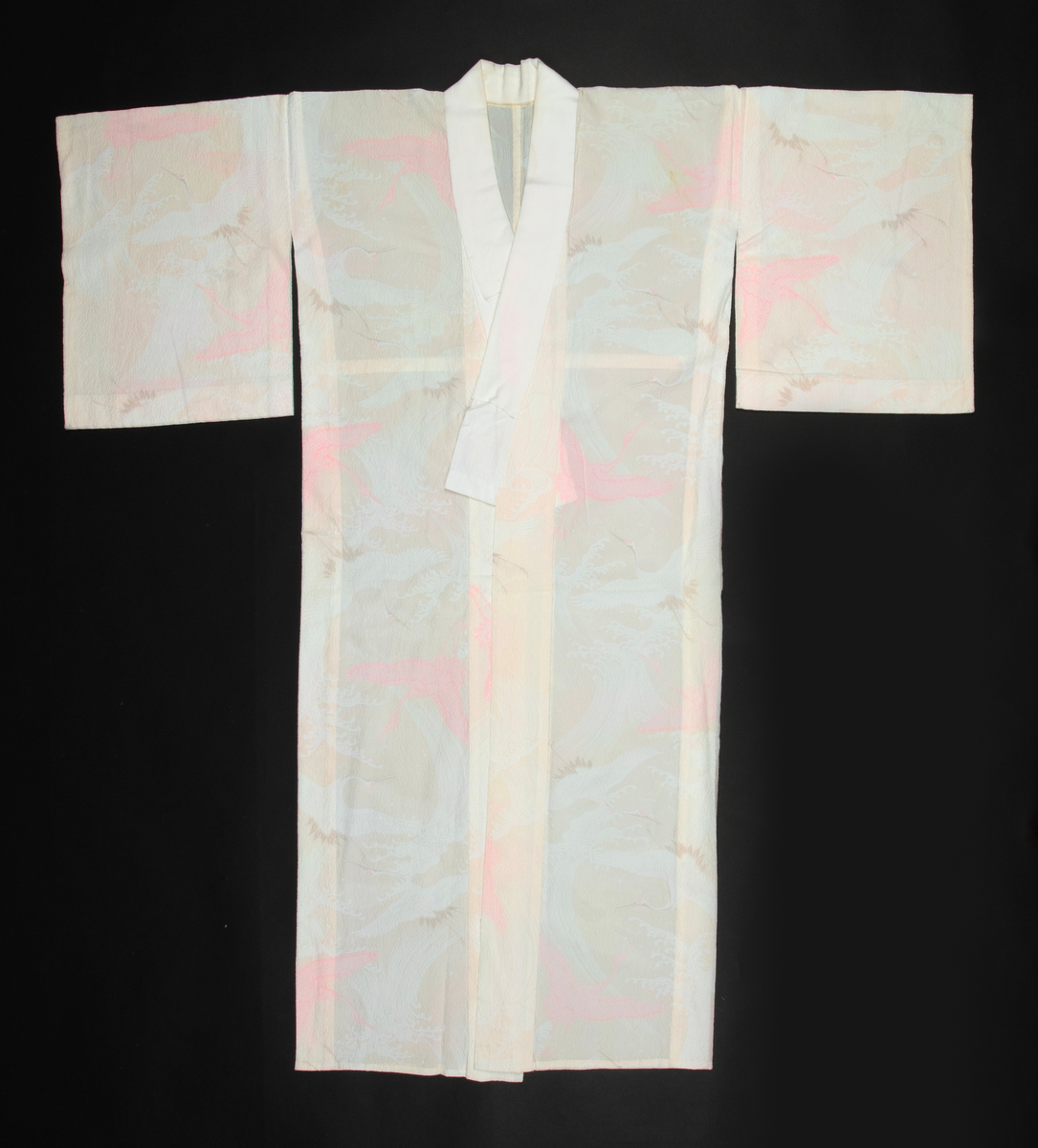 Antrekk som består av en ikatvevd kimono med jakke (haori) i mørkeblå, tynn ull med geometrisk mønster i blått, rødt, hvitt og gult og en underkimono (nagajuban) i rosa og hvit silkekrepp med mønster av traner og bølger. Øvre del av jakken er fôret med hvit, mønstret silkestoff. Tilbehøret består av to knyttebånd i rosa, vevd silke (Ginde-bånd), et reserve-kragestykke (hanori) i silkekrepp til underkimonoen og en elastisk strikk med metallklips til dandering diagonalt over brystet for at plaggene skal sitte pent under. Det følger med et par sokker (tabi) i hvit silke med metallspenner og bomullsfôr og et par sko av geta-typen i svart plast og rødt og hvitt kunstskinn med skinnsåler. To stoffstykker i samme stoff som kimonoen og underkimonoen, antagelig til reparasjon av plaggene.