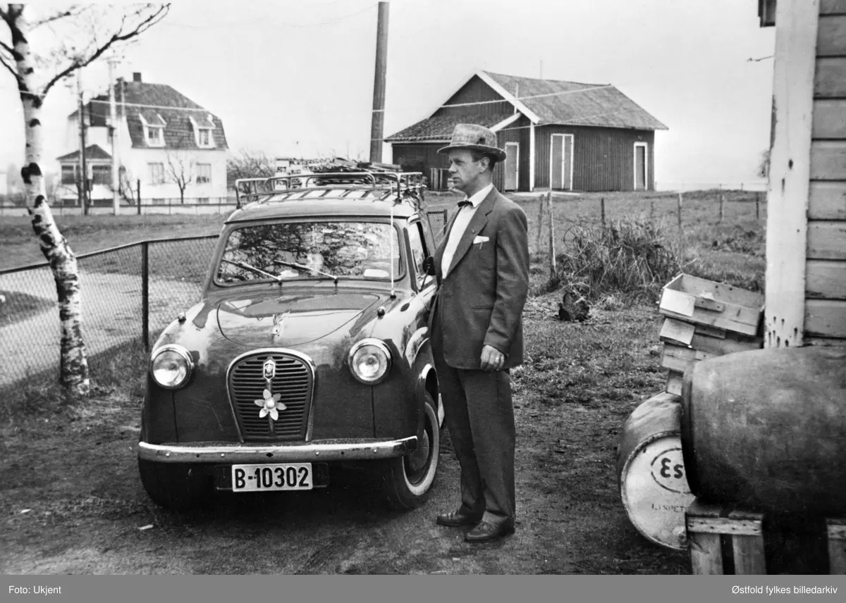 Hans Bakker med ny Austin A 35. Kirkeveien 17 på Rolvsøy 16. mai 1957. Bilkjennetegn B-10302, maiblomst i fronten på bilden. Bildet er tatt fra Kirkevein. Jernbanen går mellom det hvite huset og uthuset. 
Bakker står i innkjørselen til sin landhandel. Faren hentet fisk på brygga i Fredrikstad. Når forretingen åpnet hadde moren Paula laget ferdige fiskekaker for salg. I fatene var det parafin. Den ble punpet opp fra fatene til en glassbeholder i uthuset, 5 eller 1 liter. Veien til venstre førte over jernbanen. Nå stengt av NSB. Der uthuset i bakgrunnen står ligger nå bolig med adresse Kirkeveien 19.