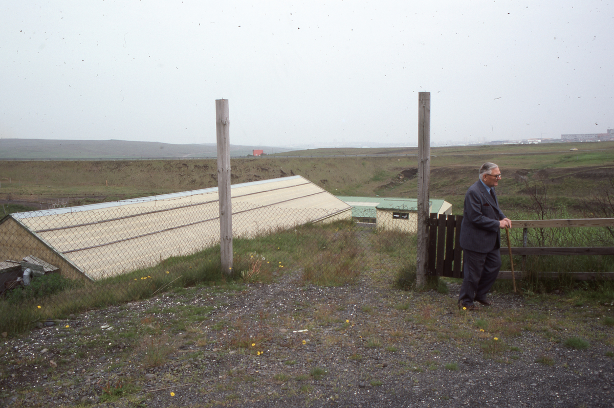 Island : Ukjent mann, han står ved et gjerde, en bygning bak han