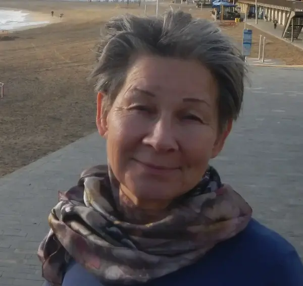 Fotografi av ei kvinne som ser rett i kamera. Hun smiler avslappet, hun har kort grå/mørkt hår og et skjerf rundt halsen.