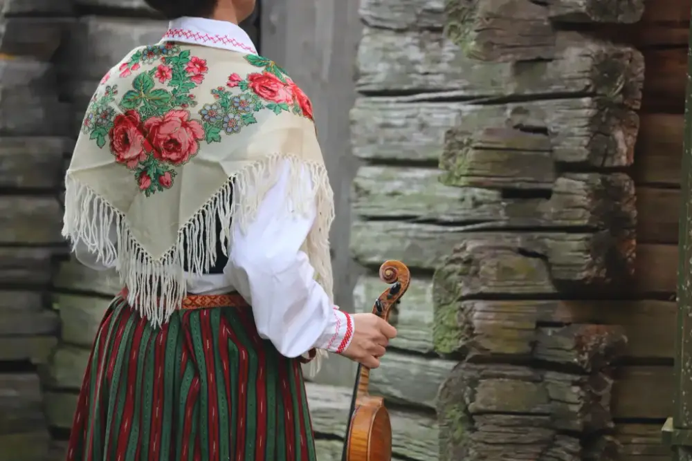 Kvinna i folkdräkt står med ryggen mot kameran och håller en fiol i högerhanden.