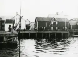 Gjesvær. Det gamle Nissenbruket og deler av bebyggelsen. Flere personer på kaia.