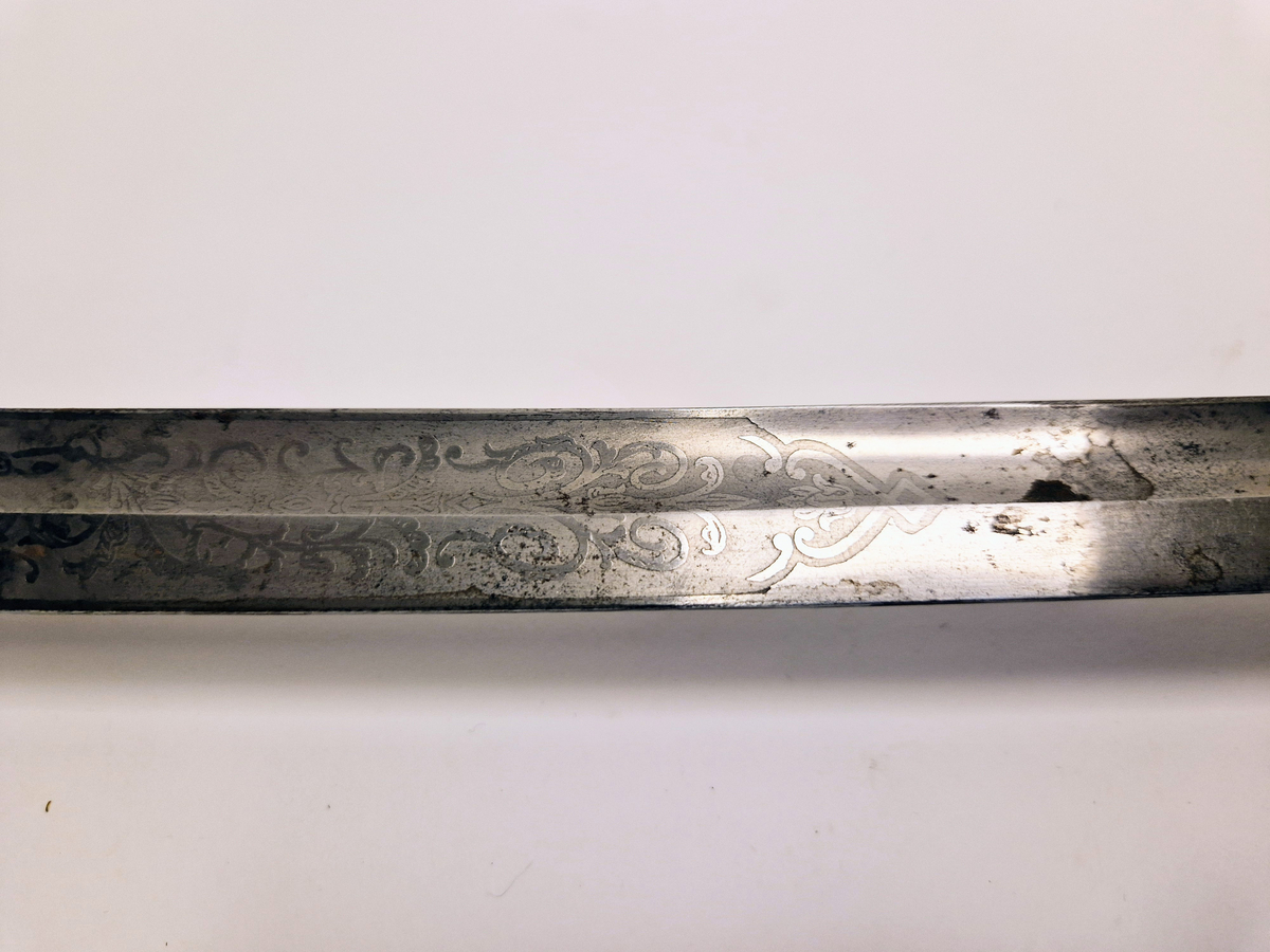 Sabel med svakt buet klinge som er dekorert med ornamenter. Grepet er i sølvfarget metall formet som riller med flettemønster og på oversiden er det messingbeslag som er festet til en buet parerbøyle, også i messing.  Parerstang med bergmannssymbolet (hammer og bergsjern). Balg av sort skinn med messingbeslag og ringer hvor det er festet skinnremmer med spenner for å feste sabelen til et belte. Spennene er støpt med løvehodemotiv. Rundt håndtaket er det tredd et bånd av metalltråd som har en kule i enden.