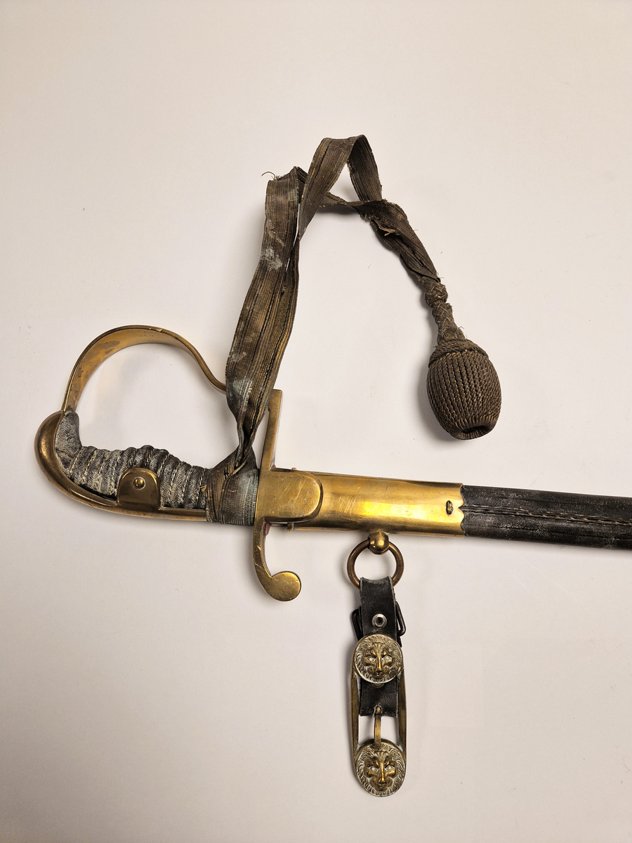 Sabel med svakt buet klinge som er dekorert med ornamenter. Grepet er i sølvfarget metall formet som riller med flettemønster og på oversiden er det messingbeslag som er festet til en buet parerbøyle, også i messing.  Parerstang med bergmannssymbolet (hammer og bergsjern). Balg av sort skinn med messingbeslag og ringer hvor det er festet skinnremmer med spenner for å feste sabelen til et belte. Spennene er støpt med løvehodemotiv. Rundt håndtaket er det tredd et bånd av metalltråd som har en kule i enden.