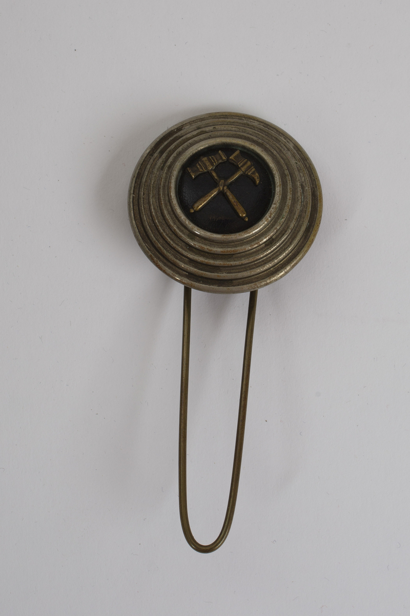 Tradisjonel tysk bergmannshatt, "Schachthut" til paradeuniform. Trukket med fløyel. Merke i metall med hammer og jern-symbolet og en krans med sløyfe foran. Gullfarget bånd rundt toppkanten. Fjærbusk med hvite og sorte fjær. Feste til denne er i metall og har en rund knapp med hammer og jern-symbolet. Hatten har et hull på venstre side hvor denne stikkes nedi. Foret med lyst silke(?)stoff. Svettebånd av brunt skinn.