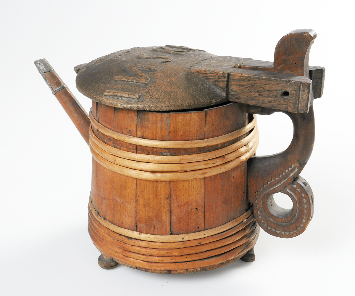 Strutkanna av trä. Laggad kanna med pip. I pipens infattning av tenn. Lock och handtag utsmyckade med tandornamentik. På locket står bosktäverna I N S K P D i relief. Kannan står på tre kulfötter - den ena till hälften av. I botten en lapp skriven av G.O. "Struta-kanna från Lädja Bergs socken Wärend 1865."

Inskrivet i huvudbok 1867.