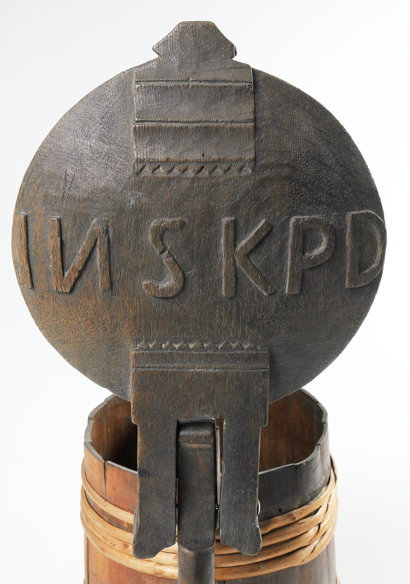 Strutkanna av trä. Laggad kanna med pip. I pipens infattning av tenn. Lock och handtag utsmyckade med tandornamentik. På locket står bosktäverna I N S K P D i relief. Kannan står på tre kulfötter - den ena till hälften av. I botten en lapp skriven av G.O. "Struta-kanna från Lädja Bergs socken Wärend 1865."

Inskrivet i huvudbok 1867.