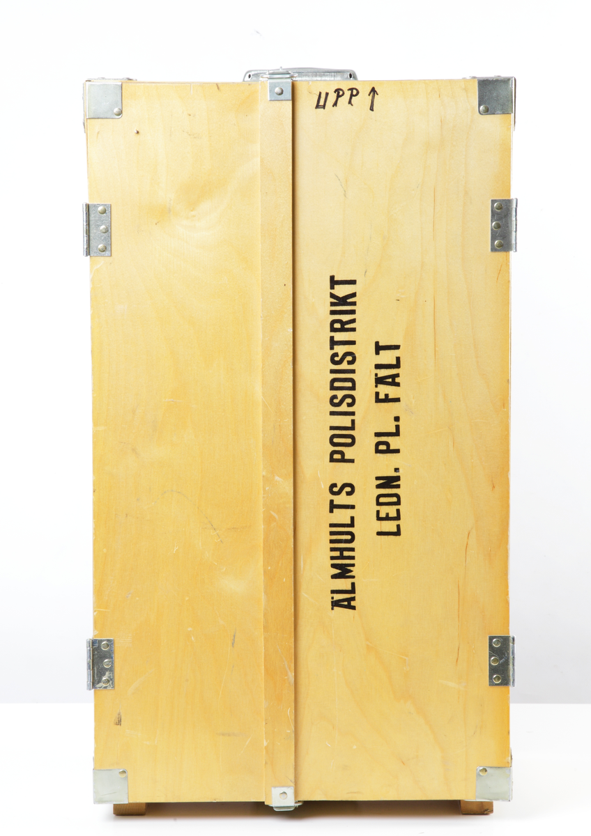 Rektangulär låda i lackad plywood med stålskodda hörn och kanter. Gavlarna försedda med bärhandtag och lås i förzinkad pressad plåt. Lådan kan förvaras liggande, men kan även ställas upp som skåp. Botten och ena gaveln försedda med fotplattor och skenor i plywood resp. trä. Framtill finns två dörrhalvor som kan öppnas. I skåpet finns fem fack som förvaringsutrymmen. Vänsterdörrens insida har en fastskruvad lampa som koplas till ett cigarettuttag. Här finns även tio hållare för pennor. Högerdörren har en innehållsförteckning för skåpet, och vissa adresslistor fästa med häftstift. Lådans utsida märkt på ena dörren "ÄLMHULTS POLISDISTRIKT LEDN. PL. FÄLT", och i botten "AB PLYFA MALMÖ".

Lådan innehåller i översta facket till vänster: en ficklampa märkt Durabcam, fäst med spännmand i lådan, plastlåda innehållande knappnålar, småspik, 14 färgkritor, tavelkritor, tre suddgummin, en Ballografpenna och en blyertspenna.

Översta facket till höger: en skyddshandbok, boken "Grövre våldsbrott", "SamRik del 2A", "Anmälningsrutiner, "telekatalog för polis- och åklagarväsendena, rulle med pappersremsa, förpackningar, plastnålar, Primus gasolvärmare, Primus gasolplatta med tub, RX limflaska, plastlinjal, hålslag märkt Ojop, rulle med etiketter, tejprulle märkt Tesa, morakniv med fodral, gem i magnetburk, två gemaskar, en ask med häftstift märkt Olfa, stämpeldyna märkt Artline, stämpel från Polismyndigheten i Älmhult.

Nedre facket till vänster: Pärm innehållande: Skrivblock, skrivpapper, Ansökan om ordningsvakt, Konceptanmälan, Spaningsuppslag grövre brottmål, Förhör, Förordnande av ordningsvakt, plastfickor.
Pärm innehållande: Inmönstring, listor, adresser, personal.
Pärm innehållande: Aktuellt, fall, åtgärder.

Nedre facket till höger: Pärm innehållande: Personal, Insatsgrupper.
Pärm innehållande: Polisens Räddningstjänst.
Pärm innehållande: Älmhults Polisdistrikt, rulle med pappersremsa.

Bottenhyllan: Kastrull med lock, köttbuljong, snabbkaffe, teförpackning, 30 plasmuggar, ca 15 plastskedar, sex teskedar i stål, förbandslåda med innehåll, 10 ordningsvaktsbrickor, 10 armbindlar i svart för ordningsvakt, 9 armbindlar för Polis, en väst för Polis insatschef, ett sittunderlag ?

Insidan på vänster dörr: En sax, två blyertspennor, en färgkrita, tre tuschpennor, en lampa för cigarettuttag.

Insidan på höger dörr: Skåpets innehållsförteckning och Radio Kronobergs larmlista.