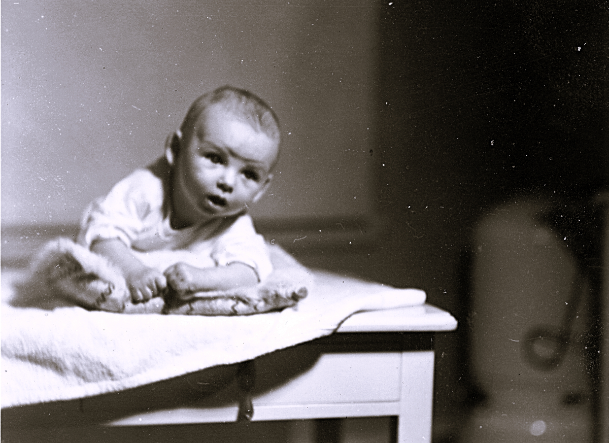 Foto av baby som ligger på mage med kudde under sig. Text baksida kort: "Heja grabbar här kommer Per Olof Skärgård".