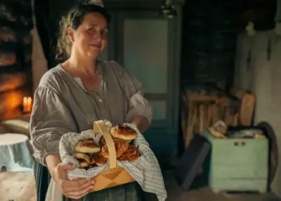 Kvinne i historisk miljø holder en kurv med nybakte boller.