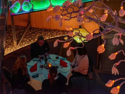 En liten grupe voksne spiser middag ved et lite rundt bord. Bildet er tatt i fugleperspektiv