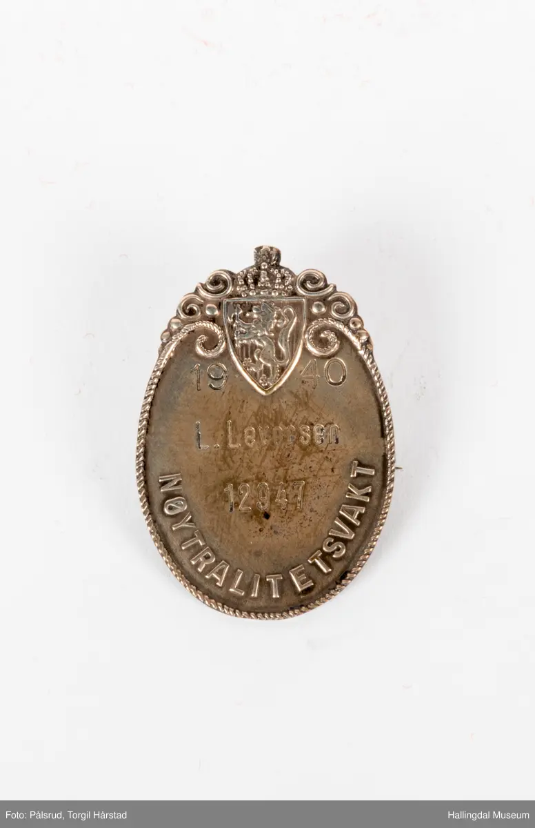 Nøytralitetsvaktmerke, 1940. Tilhørt Leif Levorsen med nummer 12947. Merket har en oval form med en bord som er ornamentert rundt riksvåpnet øverst. Navn og nummer står i midten.