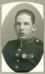 En ung man i uniform (m/95) med förtjänstmärken.
Bröstbild, halvprofil. Ateljéfoto.