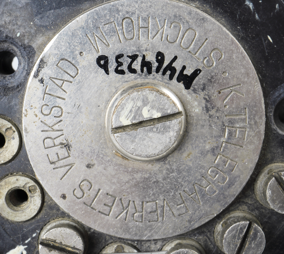Bordstelefon av Televerkets modell 1892. Bestående av en svartmålad, gulddekorerad ram av plattjärn. Samt däruti infästad en signalgenerator med förnicklad vev och svart knopp. Luren har en svart böjd taltratt samt en samtalsbrytare/sekretessanordning utformad som en svart tangent. Klykan som luren hänger i är förnicklad. Hela telefonen vilar på fyra svarvade tassar av trä. Kabeln mellan luren och spolarna är ljusbrun och tygspunnen.