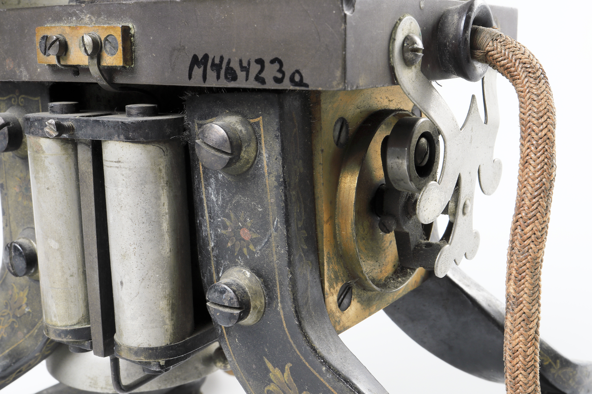 Bordstelefon av Televerkets modell 1892. Bestående av en svartmålad, gulddekorerad ram av plattjärn. Samt däruti infästad en signalgenerator med förnicklad vev och svart knopp. Luren har en svart böjd taltratt samt en samtalsbrytare/sekretessanordning utformad som en svart tangent. Klykan som luren hänger i är förnicklad. Hela telefonen vilar på fyra svarvade tassar av trä. Kabeln mellan luren och spolarna är ljusbrun och tygspunnen.